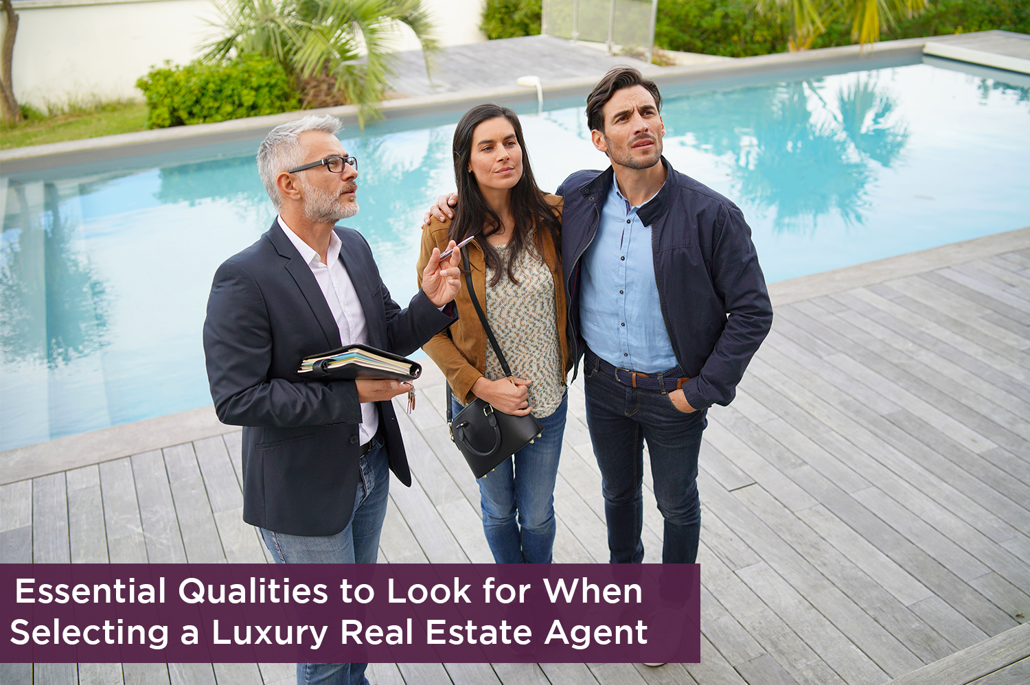 A luxury real estate agent standing outside with two clients in front of a pool, looking at a luxury home.